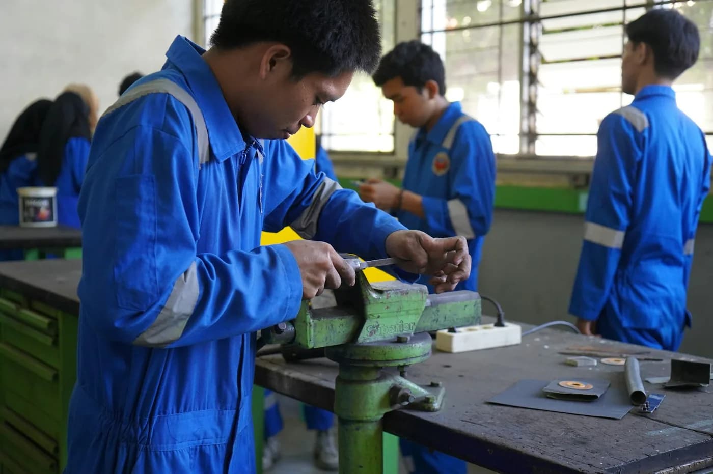 Engineering students shaping metal parts at a workshop bench